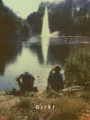 A serene image captures two figures seated near a body of water, likely a lake or pond, with a towering fountain dominating the background. The scene is set during daylight, indicated by the natural light and the soft color palette, which includes greens, blues, and browns. A layer of text, "Grief," is added to the bottom.