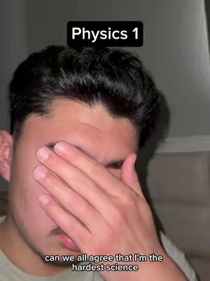 A medium shot of a young man covering his face with his right hand, implying stress or frustration. Above his head is a black rectangle with white text that says 'Physics 1'. Below is a line of white text visible at the bottom of the frame.