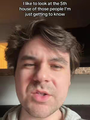 A close-up shot of a man's face, likely indoors. The man has short, dark brown hair and is looking directly at the camera. The background is out of focus, with a glimpse of what appears to be a light source or window.