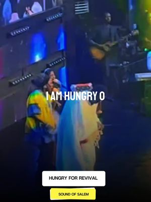 The image shows a live performance on stage. The stage is lit with blue and green lights and there are people on stage, including singers and musicians. Text overlays are added to the image.