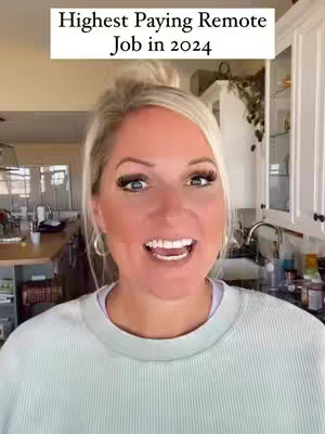 A woman with blonde hair and makeup smiles and speaks directly at the camera. Behind her is a kitchen with white cabinets and appliances, and visible greenery.