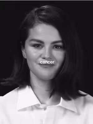 A grayscale close-up of a person's face, prominently featuring the word "cancer" overlaid on the lower part of the face. The person's hair is dark and frames the face, and they are wearing a light-colored shirt.