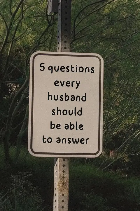 The image features a white rectangular sign with a rounded border. The sign is attached to a metal post and displays black text that reads: "5 questions every husband should be able to answer."