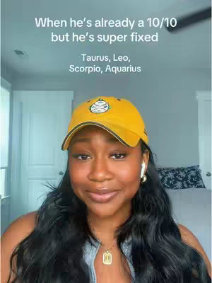 A woman in a yellow baseball cap and a light gray top looks directly at the camera against a pastel background. Text overlay on the top describes the content subject. The woman has dark hair, some of which is tucked behind her ears, and is wearing a simple gold necklace and white ear pods. The background is a light blue and a plain pale beige wall in the background.