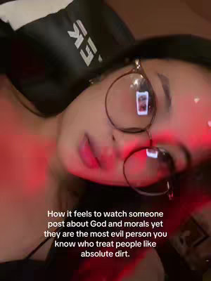 A close-up shot of a person wearing glasses, looking towards the camera. The image has a warm color tone, with red lighting across the face. Text overlayed at the bottom reads, 'How it feels to watch someone post about God and morals yet they are the most evil person you know who treat people like absolute dirt.'