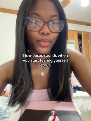 A dark-skinned woman with long, dark hair and glasses looks towards the camera. She is wearing a light pink top and a necklace. The image has overlaid text at the bottom, and the overall tone is warm, using natural lighting, possibly indoors.