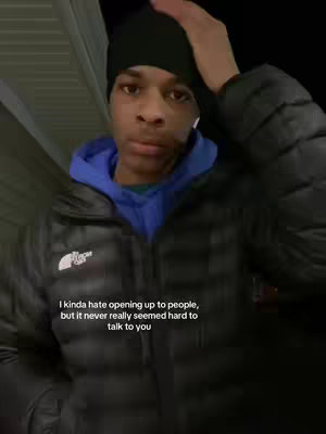 A young man is captured in a medium shot, posed outdoors. He's wearing a black beanie, a blue hoodie, and a black puffy jacket. His right hand rests on his head. Text overlayed on the image reads, "I kinda hate opening up to people, but it never really seemed hard to talk to you."
