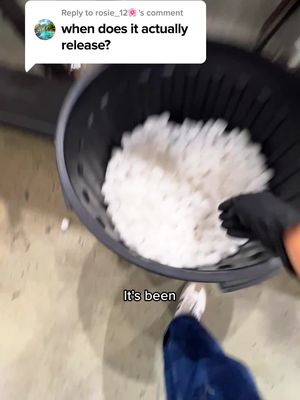 The image shows a person's feet and legs, with blue jeans and white sneakers. They are standing near a large black container filled with a white, amorphous substance, possibly foam or small pellets. Black gloved hands reaching into the foam for a better look. A comment box with the question 'when does it actually release?' appears on the left. A text overlay at the bottom reads 'It's been'.