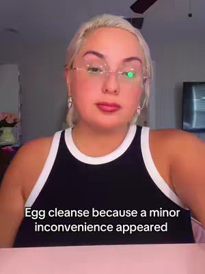 The cover image features a woman with blonde hair wearing glasses and a black tank top. Text at the bottom overlay reads, 'Egg cleanse because a minor inconvenience appeared'. She is looking at the viewer with a neutral expression.