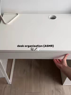 The cover image shows a section of a clean, white desk. The desk has a hole for wires and a drawer handle. A hand is visible, pulling the drawer open. The background is a muted wooden floor. The text overlay reads 'a desk organization (ASMR)' in a block font..