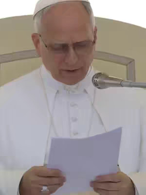 The cover image shows Pope Leo, dressed in white, speaking into a microphone while holding papers. He is wearing glasses and a white skullcap. The background suggests an outdoor setting, possibly a general audience.
