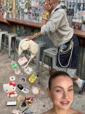 A selfie style shot with a woman's face in the foreground, she is smiling, and behind her are the items she took out of her bag.