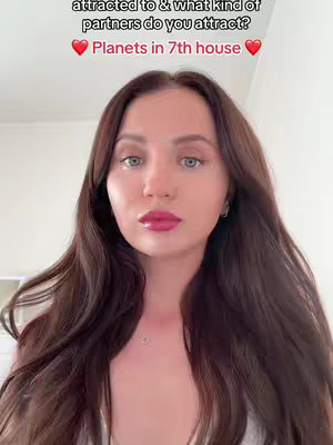 A selfie-style cover image featuring a light-skinned woman with long brown hair. She is looking directly at the camera with a neutral expression. She has full, red lips, and wears a simple necklace. The background is a clean white wall. Superimposed at the top is white text that asks about the 7th house in astrology, with red heart emojis on either side of a phrase. The overall composition is straightforward, focusing on the woman's face.