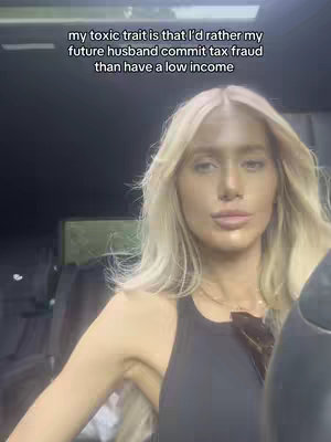 A woman with long blonde hair is centered in the frame, set against a dark interior that is possibly a car. Above her, text overlays appear, addressing a 'toxic trait' related to financial attitudes in a relationship.