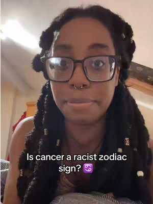 A woman with braided hair and glasses looks directly at the camera with a neutral expression. Text overlayed on the image asks, 'Is cancer a racist zodiac sign?'