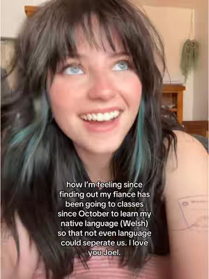 A young woman looking upwards with a smile, her dark hair styled with a side part and blue highlights. Text overlaid at the bottom details her feelings about her fiance learning Welsh.