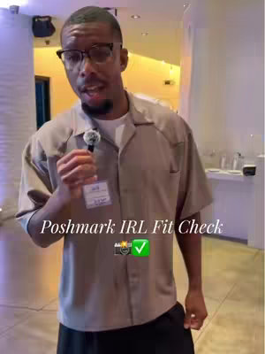 A man wearing glasses and a light brown shirt with a microphone clipped to it stands and presents to the camera. Text overlaid on the image reads 'Poshmark IRL Fit Check'. A camera and checkmark icon graphic is also present.