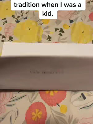 A close-up shot shows a white, rectangular item partially obscuring the view. The background is a floral pattern dominated by yellow and red flowers on a light-colored fabric. The text overlay reads "tradition when I was a kid."