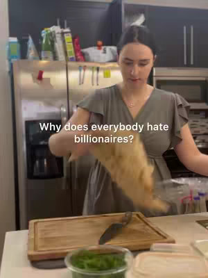 A person in a kitchen is holding a bag which looks like food. Above her is a banner that says: Why does everybody hate billionaires?