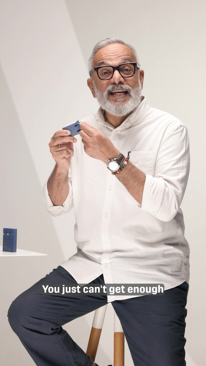 An older man with a gray beard and glasses is seated in front of a plain white background. He is holding a small blue object, like a charger, in his hands and speaking with an excited expression. A blue box is positioned to the left of him, and the text overlay 'You just can't get enough' is visible at the bottom.