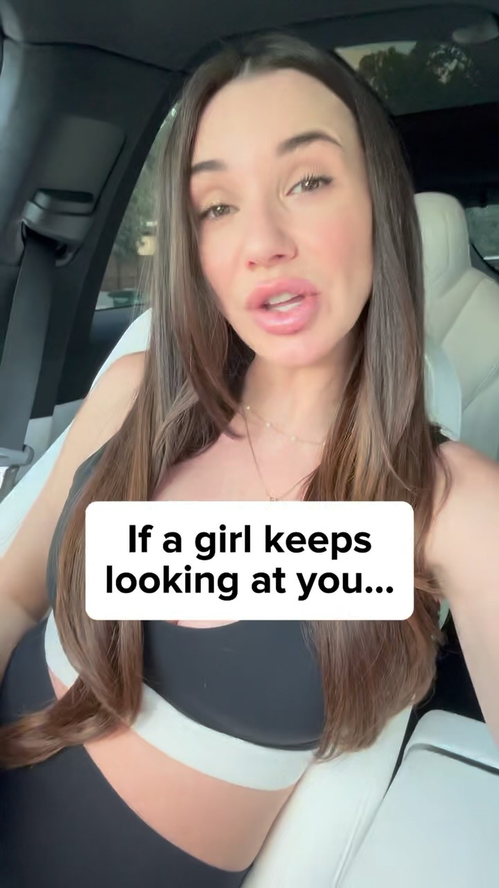 A woman with long brown hair is sitting in a car. She is looking directly at the camera and speaking. A white text overlay is visible in the bottom center of the frame.
