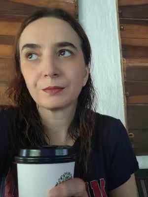 A woman is shown from the chest up, gazing upwards. She has long, dark hair and is holding a coffee cup in her hands. The background includes wooden and off-white architectural elements.