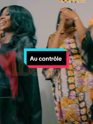 The image shows three women, captured from the chest up, seemingly in a moment of performance or celebration. The woman on the left wears a black outfit, while the middle figure, slightly obscured, dons a colorful patterned dress. The third woman on the right has an elegant yellow shawl. The background is plain and light-colored. Overlaid on the image is a teal and black rectangle displaying the text 'Au contrôle'.