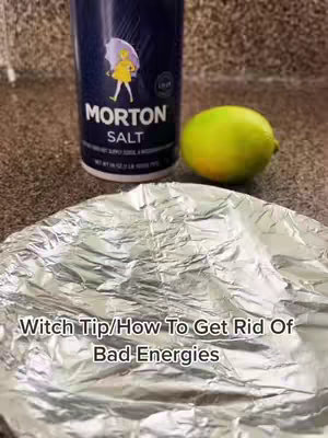The cover image displays a close-up shot of a wrinkled aluminum foil sheet on a countertop. In the background, to the right of center, are a lime and a container of Morton Salt. The top of the salt container is visible, with the brand name and logo clearly displayed. The background appears to be a light-colored, possibly tiled or stone countertop. The text overlay is white, and it reads "Witch Tip/How To Get Rid Of Bad Energies".