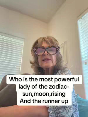 A woman with blonde hair and glasses is centered in the frame, and the background is a bright room. There's a text overlay at the bottom of the frame.