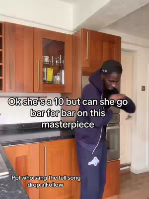 A man in a kitchen is bent over to his right and has his arms bent in what appears to be a dancing pose. The image is centered and the man is wearing a dark zip-up hoodie and dark sweatpants. On the top portion of the screen white text is displayed. The text is over-laid onto the image.