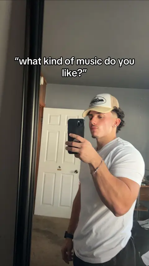 A man in a white t-shirt and a cap is taking a selfie in front of a mirror. The background includes a door and a wall. The hook text is overlayed on the image. The overall composition is focused on the man, suggesting a casual, lifestyle-oriented video.