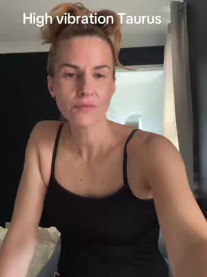 A woman with blonde hair pulled up in a messy bun stares directly at the camera. The background shows a blurred interior.