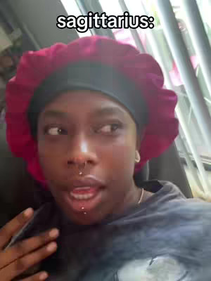 A selfie-style shot featuring a person with dark skin, looking off to the side with a slight smile. The person wears a burgundy bonnet and a grey shirt. The words "sagittarius:" are superimposed on the top of the image.
