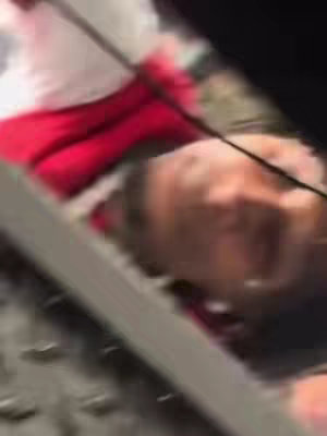 The image shows a person looking upward while partially obscured by a bright surface. The person is wearing a red garment. The perspective is from a low angle, looking up.