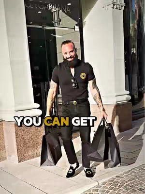 A man in all-black attire, carrying shopping bags, stands in front of a high-end store entrance. The image focuses on his confident stance and the luxury setting.