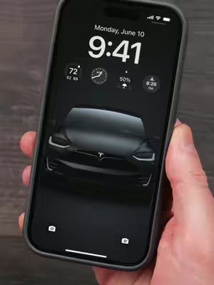 The cover image shows a hand holding an iPhone displaying a black Tesla car live wallpaper on its screen. The phone screen shows the time, date, weather, and battery percentage. The background appears to be a dark, possibly wooden surface.