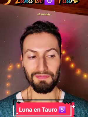 The cover image features a man with a beard and short, dark hair, centered in the frame. He is wearing a blue sweater. The background is blurred, but hints of fairy lights and a wall are visible. Text overlays include "Luna en Tauro" in a red and black bar at the bottom and smaller text at the top of the frame. The overall composition is a medium close-up, focusing on the man's face and upper body.