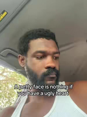A selfie-style shot featuring a dark-skinned man inside a vehicle. He is wearing a white undershirt and has a dark beard and mustache. Text overlayed on the image reads 'A petty face is nothing if you have an ugly heart'.