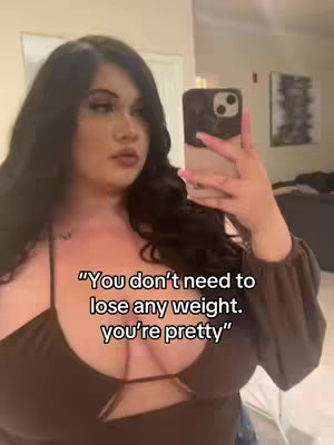 A woman is taking a selfie in a well-lit room. The caption is overlaid on the bottom of the image. The woman is wearing a brown top and the phone is slightly angled.