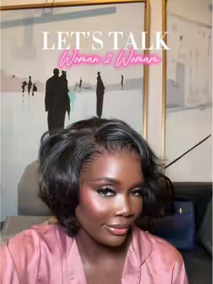 A woman with a short, dark hairstyle is the focal point, positioned slightly off-center. She wears a pink robe, and her face is well-lit with makeup, including prominent eye shadow. Behind her is a painting, with a blurred artistic representation of figures and various shades of white, gray, and black. Text overlays the image with the words "LET'S TALK Woman 2 Woman."