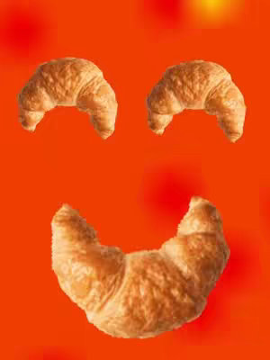 The cover image shows an orange background upon which three croissants are arranged to form a smiley face. Two croissants are positioned at the top to represent eyes, and a larger croissant forms the smiling mouth at the bottom.