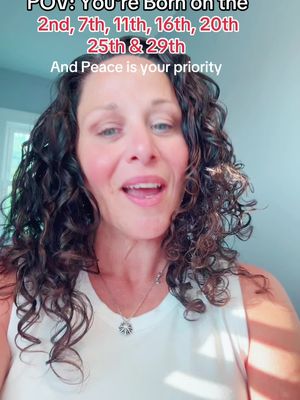 A woman with curly hair and a white top faces the camera, speaking. Text overlays at the top list birthdates. Soft lighting and a neutral background provide context.