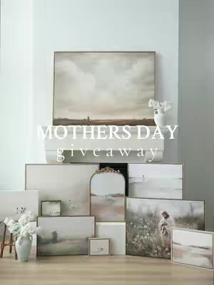 The image is a well-lit product shot featuring a white mantelpiece adorned with artwork and decorative items. At the center, a large framed canvas depicting a cloudy landscape dominates the view. Below, an array of smaller framed artwork and a mirror are artfully arranged. Flanking the artwork are vases of white flowers. The overall composition has a soft, neutral color palette with a focus on white, beige, and light gray tones, suggesting a vintage or classic interior design aesthetic.