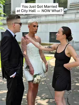 A group of three people standing outdoors in front of a building with neoclassical architecture. The main subject, in the middle, is wearing a white wedding dress and holding a small bouquet. To their left, a person in a black suit and glasses, and to their right, a person in a black top and shorts, with a tattoo on their arm. Text overlays the image.