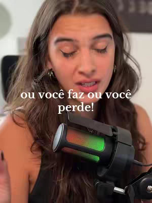 A woman with long brown hair is centered in the frame, looking slightly to the side with a concerned expression. Text overlayed on the image reads 'ou você faz ou você perde!' below the woman’s face is a multicolored microphone.