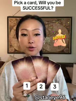 A woman with long dark hair looking directly at the camera, holding four tarot cards. Text overlaid says, 'Pick a card, Will you be SUCCESSFUL?' Numbers 1, 2, and 3 are shown on the cards. An animated graphic showing a meditating figure with the word SUCCESS above its head hovers in the background. The background consists of golden-hued artworks.