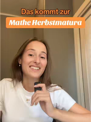 A young woman is holding a black object, likely a microphone, and smiling toward the camera. She is wearing a plain white t-shirt against a neutral indoor setting. Text overlays in orange and white that reads 'Das kommt zur' and 'Mathe Herbstmatura,' indicating a focus on math and the fall exam.