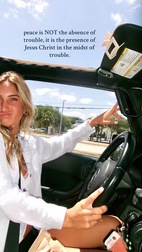 A woman with blonde hair and a white shirt is driving a car, smiling slightly and pointing with her right hand. Text overlays the image.