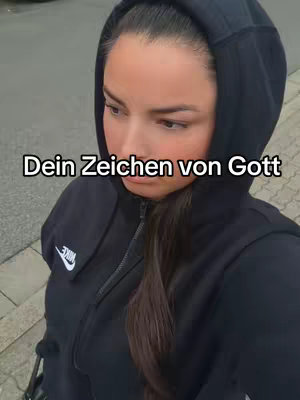 A woman in a black hoodie with the hood up, looking down. Text overlayed on the image reads 'Dein Zeichen von Gott'.