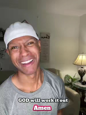 A smiling Black man wearing a white skullcap and a gray shirt is the central figure. The background includes a wall and a lamp. Text overlays read "GOD will work it out" and "Amen".
